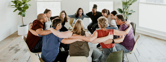 Grupo de personas sentadas en círculo con los brazos sobre los hombros de las demás